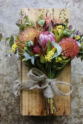 A photo of a bunch of native flowers, including eucalyptus leaves, wattle, leucospermum and proteas, bound with jute ribbon.